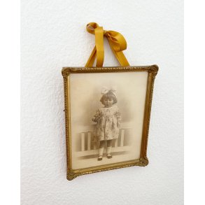 Black and white photo of a little girl in a gold frame, dated 1928